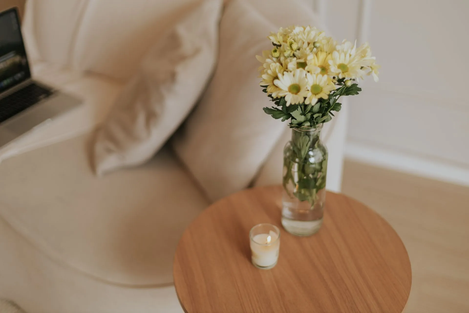 Gemütliche Wohndeko mit Blumen in der Vase und Kerze auf einem Holztisch